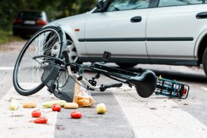 Crashed bike with spilled groceries on street near car