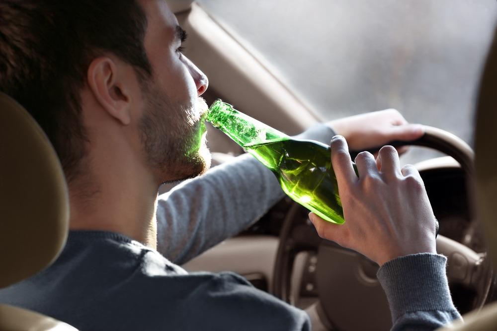 A drunk driver drinking beer from a green bottle.