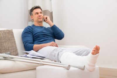 Injured man with crutches on couch talking to lawyer on phone