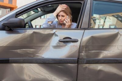 Motorist sits in damaged car on phone after accident