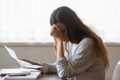 A woman holds her head in frustration as she struggles with paperwork