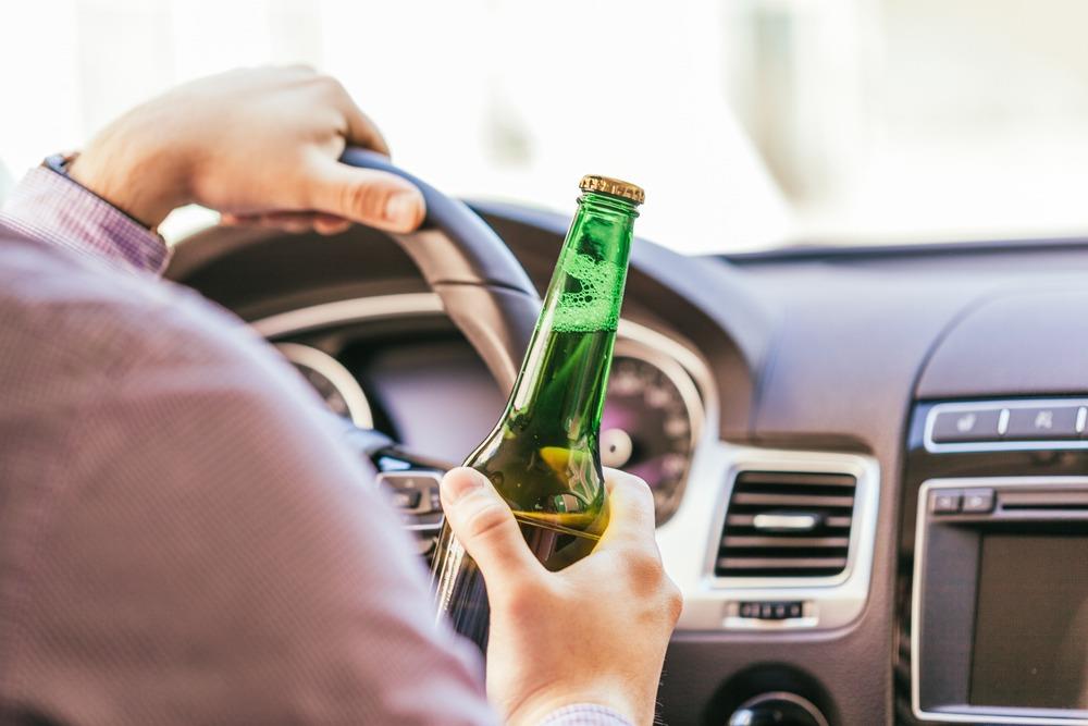 A man holds a beer while driving on the road.