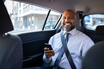 Man in back seat of car holding phone and smiling