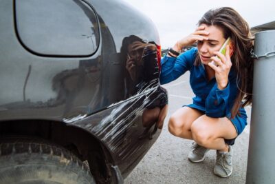 Distressed woman standing near scratched car