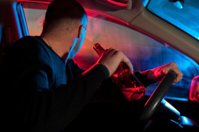 Young drunk man with alcohol bottle sitting in car