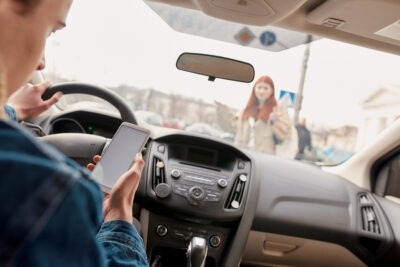 Man texting while driving as a pedestrian approaches scaled