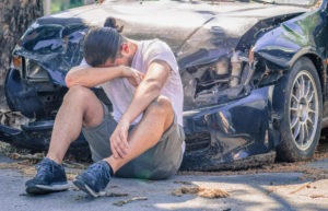 Sad man sitting in front of a totaled car