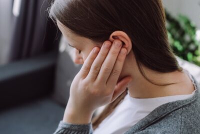 Woman holding ear suffering from tinnitus