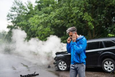 Man stand next to damaged vehicle and talks to insurer on phone about total loss threshold for cars