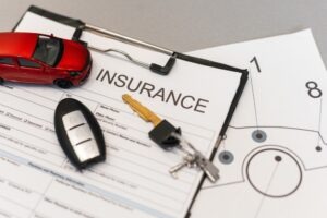 A red toy car and key fob resting on a blank form titled 'insurance,' illustrating how insurance coverage works in rideshare accidents.