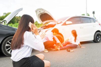 Woman on a cell phone in front of two cars asking what to do if someone is injured in an accident while driving for DoorDash.