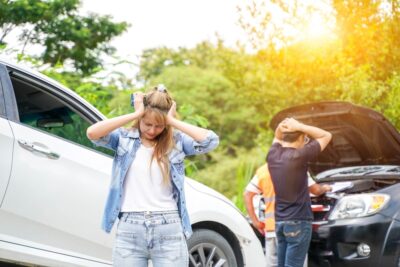 Young woman standing in front of two cars trying to figure out what to do if she has been injured while driving for Lyft