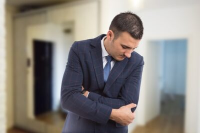 A male real estate agent in a blue suit jacket holds his arm in pain as he contemplates what steps to take after a work injury