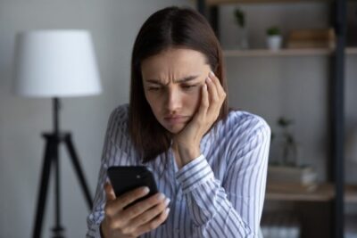 A woman frowning at her phone and wondering what to do if the workers’ comp adjuster won’t return your calls.