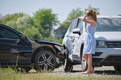 A woman standing next to two cars after a broadside collision in a common spot for them.