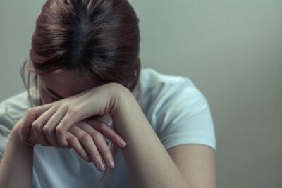 A young woman holds her head in her hands. Depression can be a sign of sexual abuse in teenagers and young adults.